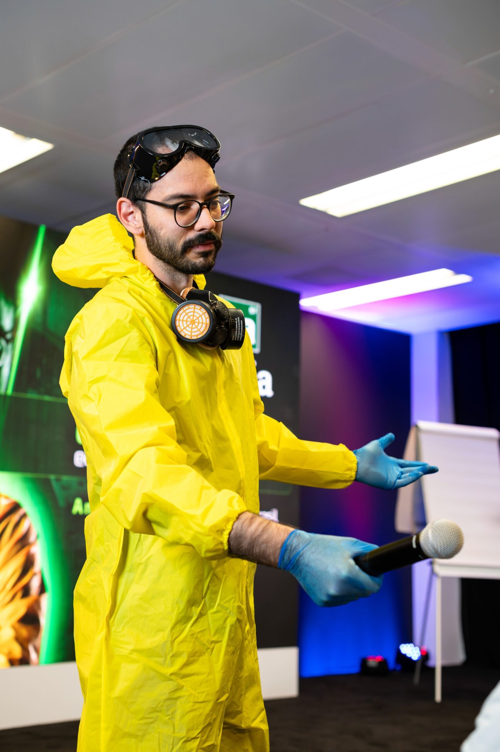 A speaker presenting on stage in a bright yellow protective suit
