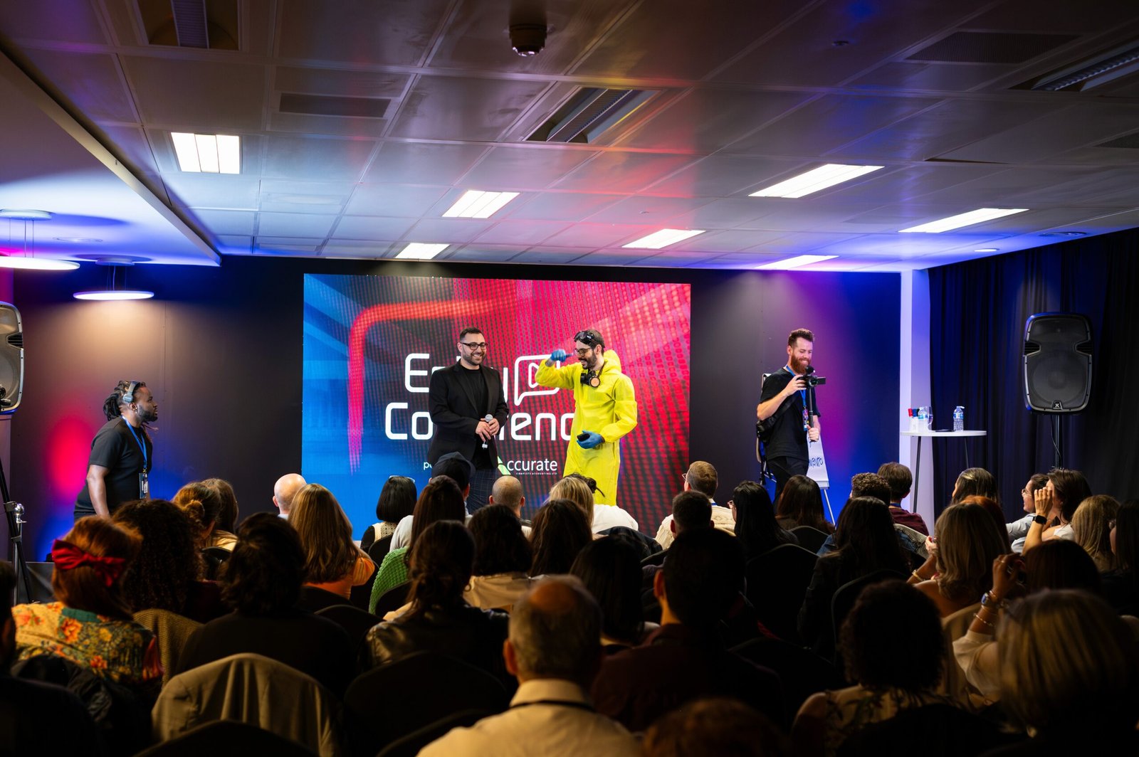 Conference audience watching a speaker on a stage lit in red and blue