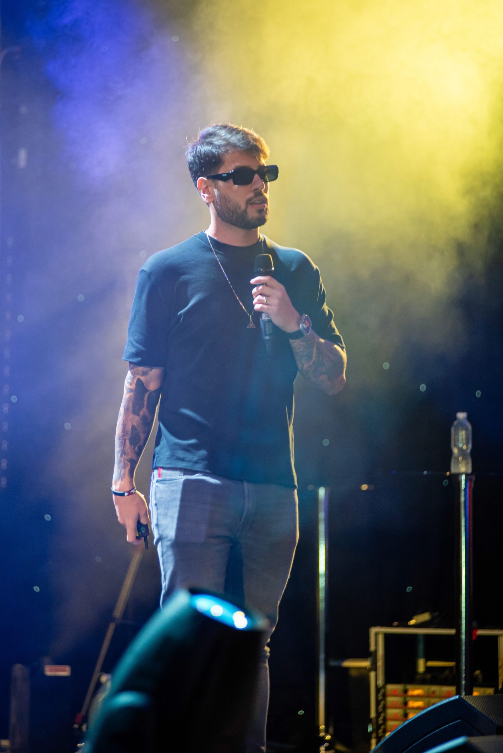 A speaker holding a microphone on a stage filled with haze and yellow backlight