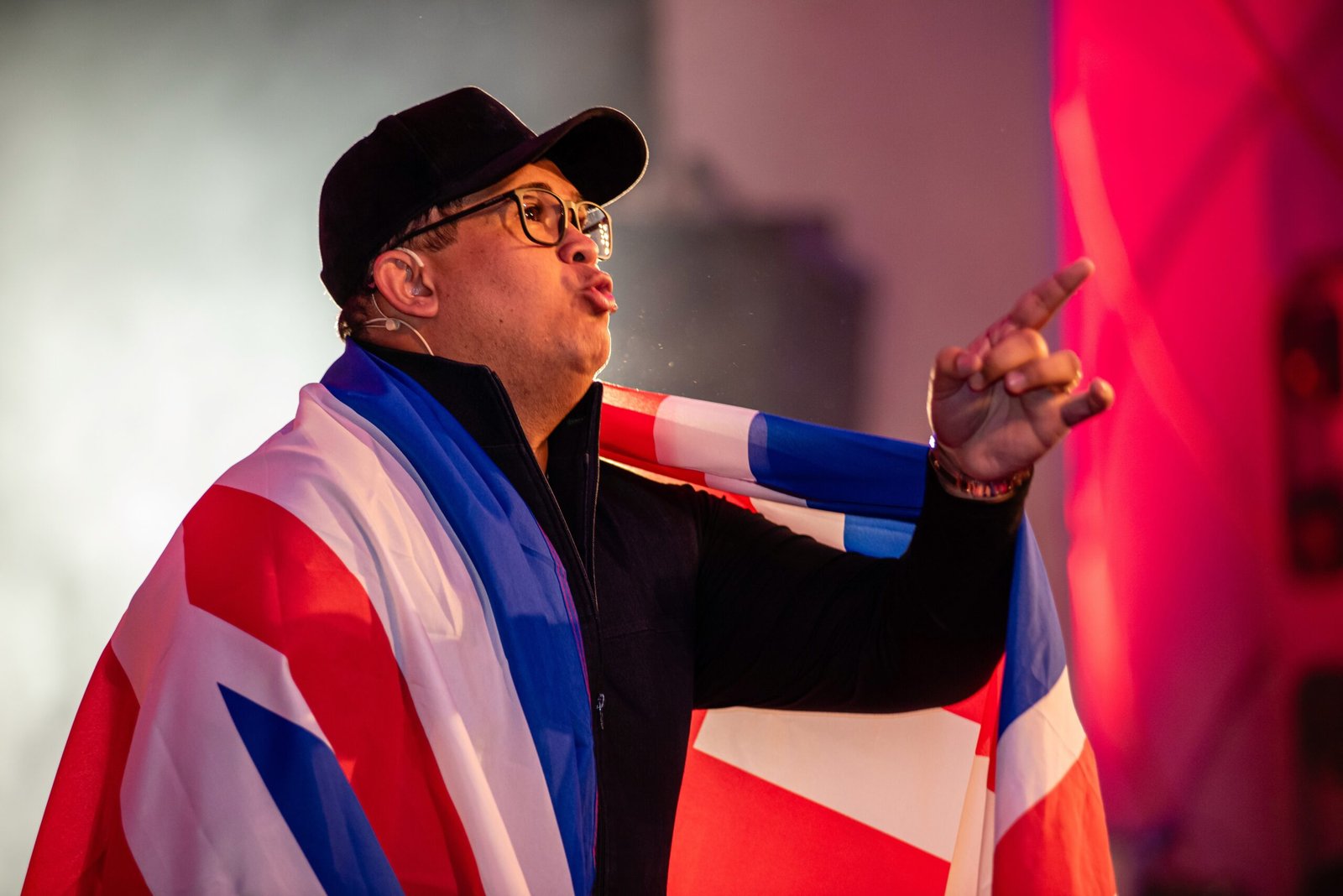 A speaker on stage draped in a Union Jack, pointing towards the audience